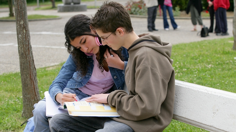 flicka och pojke på bänk som tittar i en bok utomhus